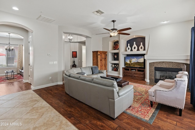 living room featuring built in shelves, a fireplace, dark hardwood / wood-style flooring, and ceiling fan with notable chandelier