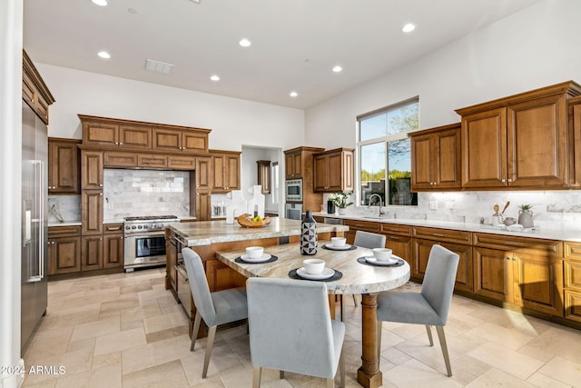 kitchen featuring sink, light stone counters, backsplash, high end stainless steel range, and a kitchen island