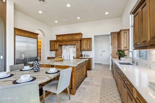 kitchen with a kitchen bar, backsplash, built in refrigerator, and sink