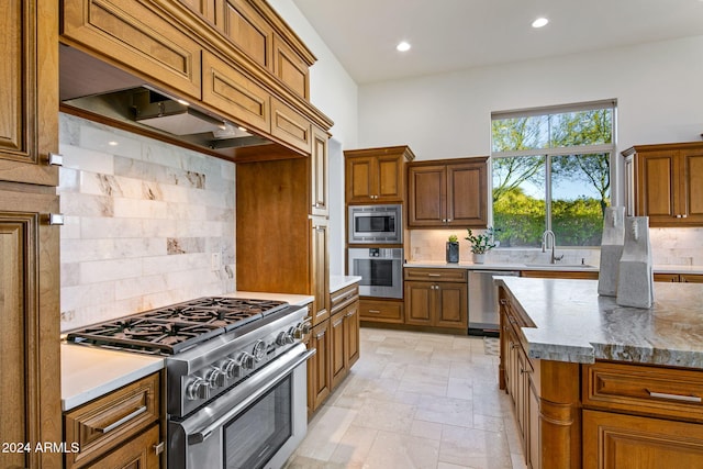 kitchen featuring sink, appliances with stainless steel finishes, tasteful backsplash, light stone counters, and custom range hood