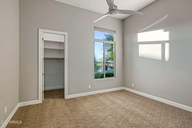 unfurnished bedroom with ceiling fan, a spacious closet, light carpet, and a closet