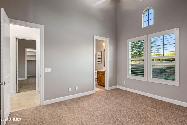 unfurnished bedroom featuring a spacious closet, ceiling fan, a high ceiling, ensuite bathroom, and light colored carpet