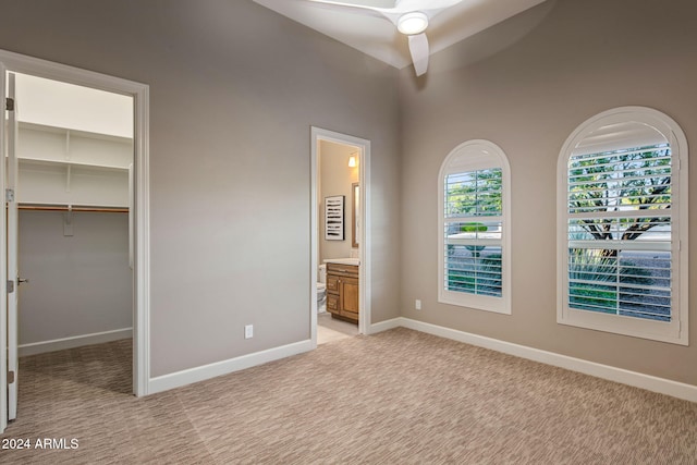 unfurnished bedroom with a walk in closet, ensuite bathroom, light colored carpet, ceiling fan, and a closet