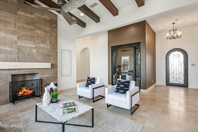 living room featuring a tile fireplace, beam ceiling, a towering ceiling, and ceiling fan with notable chandelier