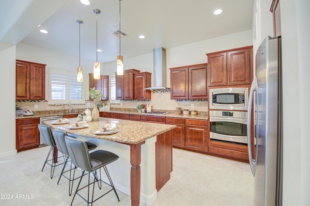 kitchen with stainless steel appliances, hanging light fixtures, wall chimney range hood, a kitchen island, and a breakfast bar