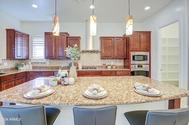 kitchen featuring hanging light fixtures, wall chimney range hood, decorative backsplash, and appliances with stainless steel finishes