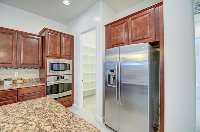 kitchen with light stone countertops, appliances with stainless steel finishes, and backsplash