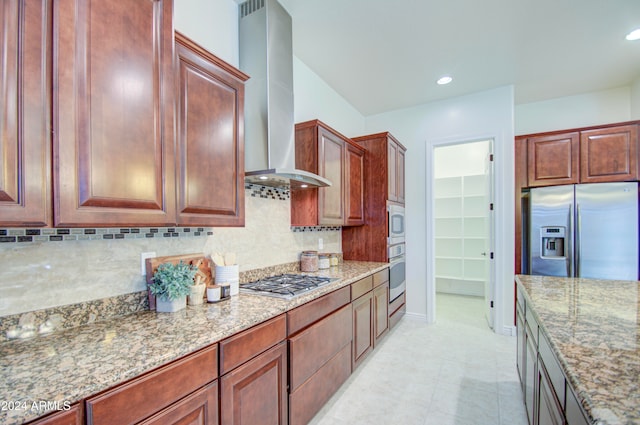 kitchen with appliances with stainless steel finishes, wall chimney range hood, backsplash, and light stone countertops