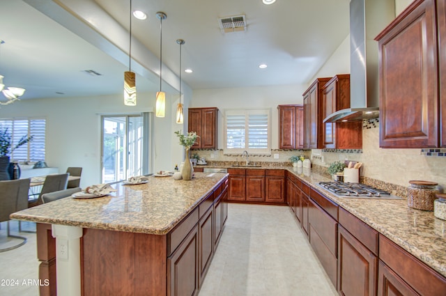 kitchen with plenty of natural light, decorative light fixtures, stainless steel gas stovetop, and wall chimney range hood