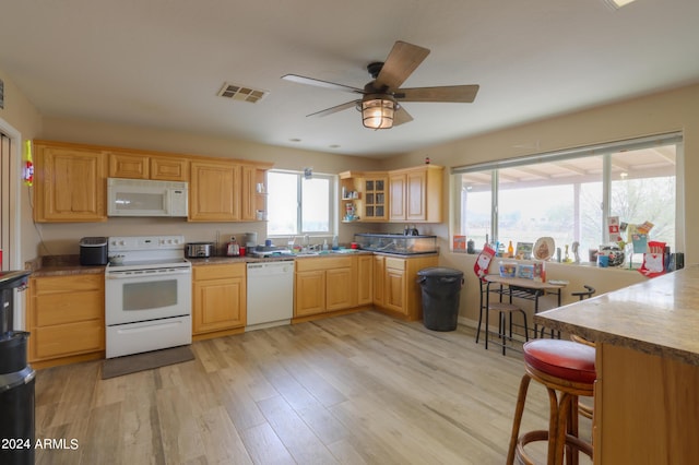 kitchen with white appliances, light hardwood / wood-style floors, ceiling fan, and a breakfast bar area