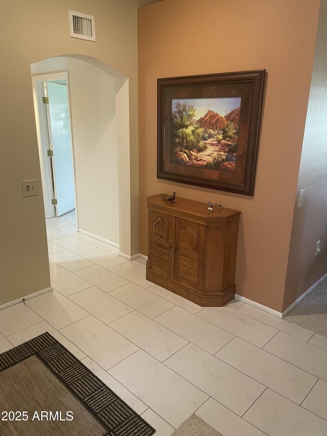 corridor with light tile patterned floors, baseboards, visible vents, and arched walkways