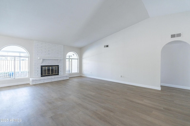 unfurnished living room with a wealth of natural light, dark hardwood / wood-style flooring, lofted ceiling, and a brick fireplace