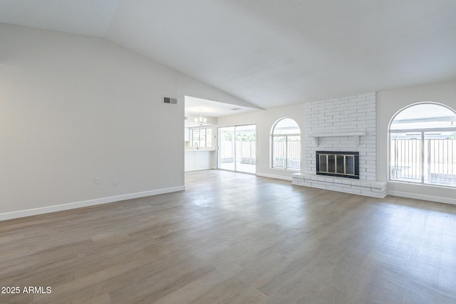 unfurnished living room featuring wood-type flooring, lofted ceiling, a fireplace, and a chandelier