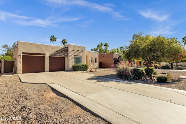 pueblo revival-style home with stucco siding, an attached garage, and driveway