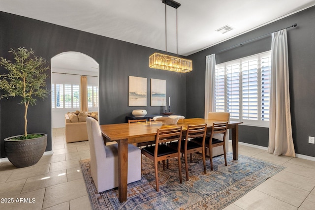 tiled dining room featuring arched walkways, baseboards, a chandelier, and visible vents