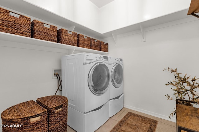 clothes washing area featuring light tile patterned flooring, laundry area, washing machine and dryer, and baseboards