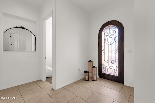 foyer entrance with arched walkways, baseboards, and light tile patterned flooring