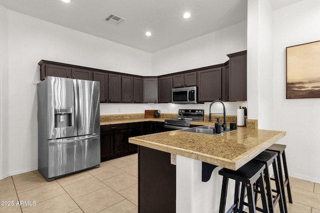 kitchen featuring dark brown cabinets, a sink, stainless steel appliances, light tile patterned floors, and visible vents