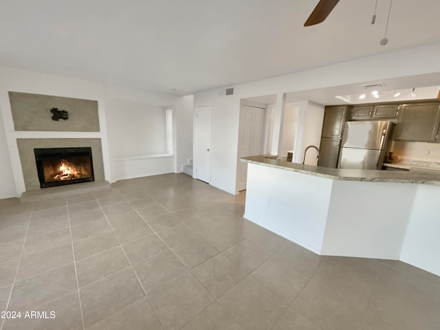 kitchen with light tile patterned floors, light stone counters, stainless steel refrigerator, sink, and ceiling fan