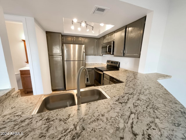 kitchen with light stone counters, stainless steel appliances, kitchen peninsula, and sink