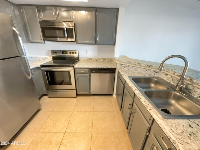 kitchen featuring gray cabinetry, light stone countertops, stainless steel appliances, sink, and light tile patterned flooring