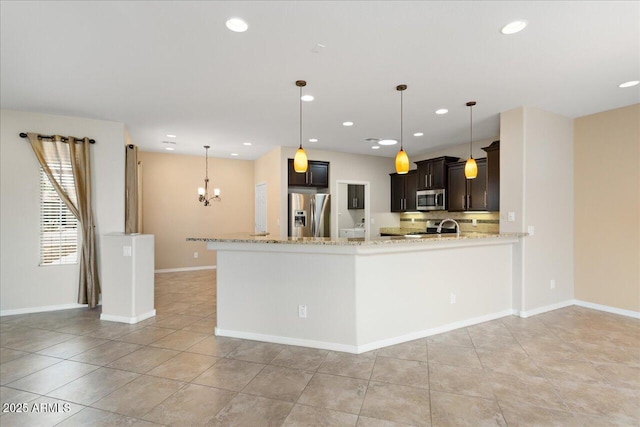 kitchen with kitchen peninsula, light stone counters, dark brown cabinets, stainless steel appliances, and decorative light fixtures