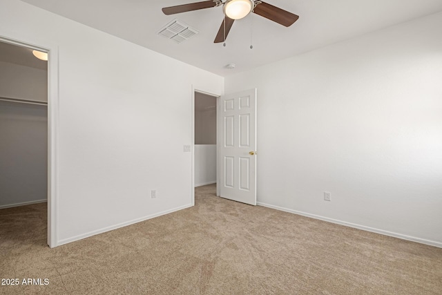 unfurnished bedroom featuring light carpet, a closet, a spacious closet, and ceiling fan