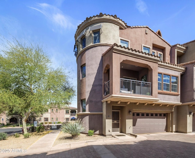 view of front of house with driveway, an attached garage, stucco siding, and a balcony