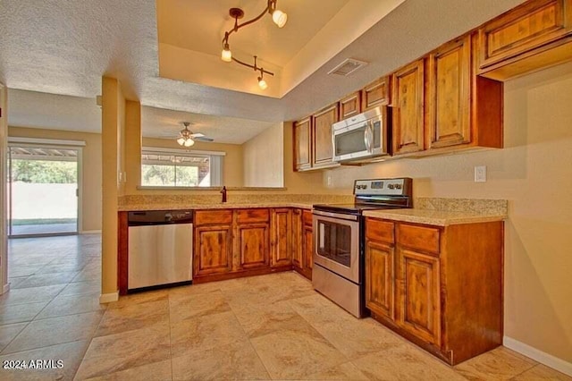 kitchen with track lighting, ceiling fan, a textured ceiling, appliances with stainless steel finishes, and a tray ceiling