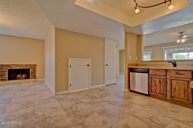 kitchen featuring stainless steel dishwasher, ceiling fan, a fireplace, and a textured ceiling