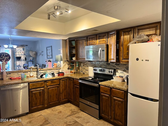 kitchen featuring light stone countertops, tasteful backsplash, stainless steel appliances, a raised ceiling, and a notable chandelier