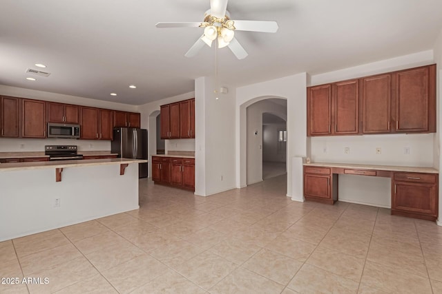 kitchen featuring light tile patterned floors, a breakfast bar, ceiling fan, appliances with stainless steel finishes, and built in desk