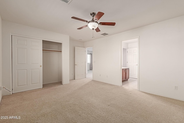 unfurnished bedroom featuring light carpet, connected bathroom, ceiling fan, and a closet