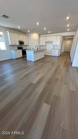 kitchen with white cabinets, an island with sink, dark hardwood / wood-style floors, and range