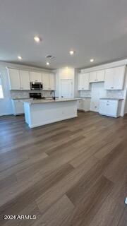 kitchen with white cabinets, a center island with sink, and dark wood-type flooring