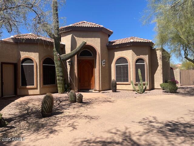 mediterranean / spanish home with fence, stucco siding, and a tiled roof