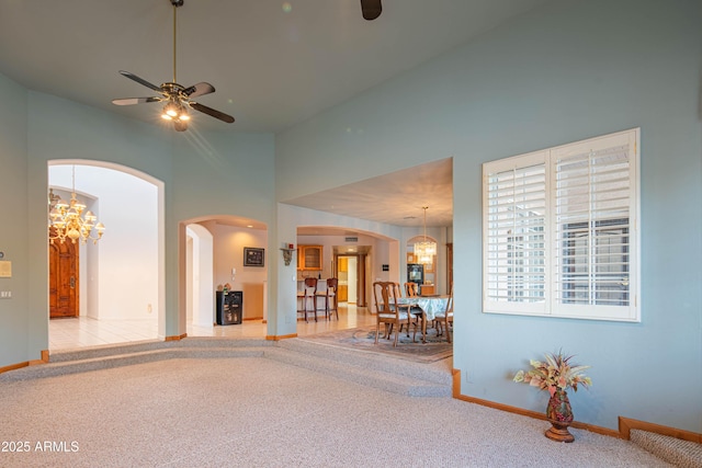 unfurnished living room with arched walkways, baseboards, ceiling fan with notable chandelier, a high ceiling, and carpet