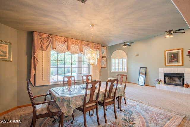 carpeted dining space featuring baseboards, a tiled fireplace, and ceiling fan with notable chandelier
