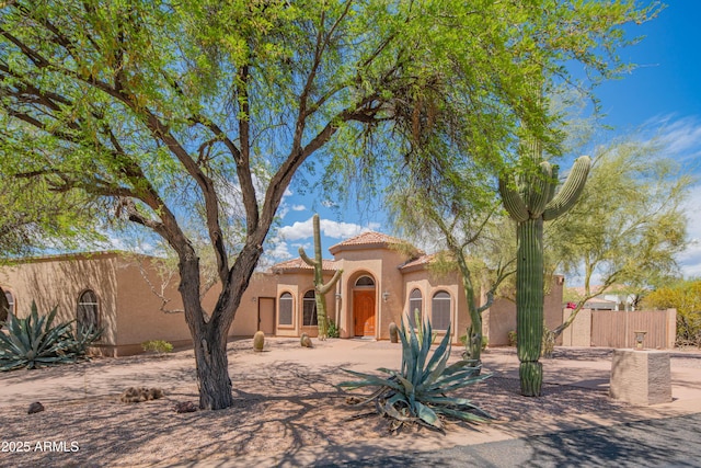 mediterranean / spanish-style house featuring stucco siding, fence, and a tile roof