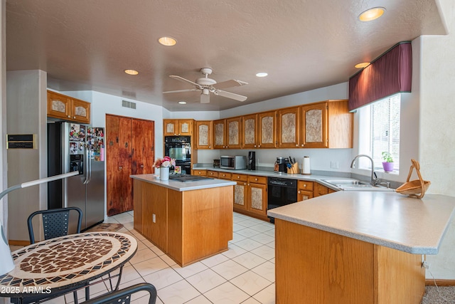 kitchen with brown cabinetry, a center island, a sink, black appliances, and a peninsula