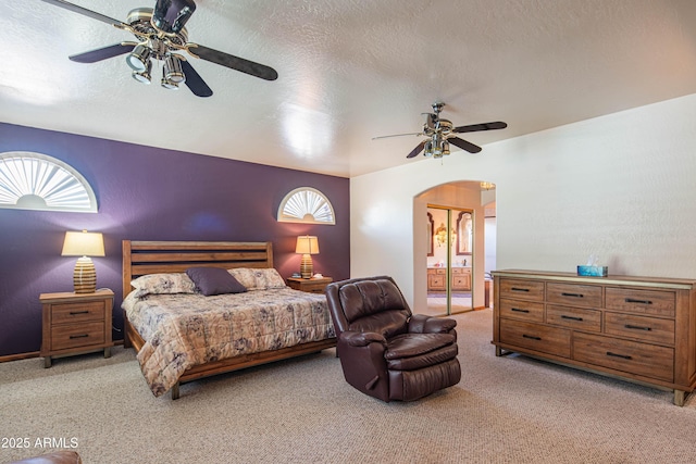 bedroom featuring connected bathroom, carpet floors, arched walkways, a textured ceiling, and a ceiling fan