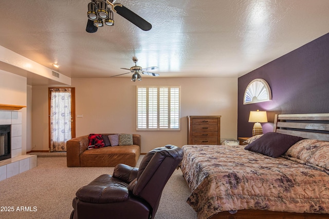 carpeted bedroom featuring a ceiling fan, a textured ceiling, visible vents, and a tiled fireplace