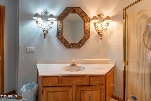 bathroom featuring a stall shower, a textured wall, baseboards, and vanity