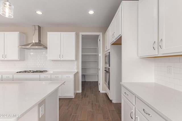 kitchen with wall chimney exhaust hood, decorative light fixtures, white cabinetry, and appliances with stainless steel finishes