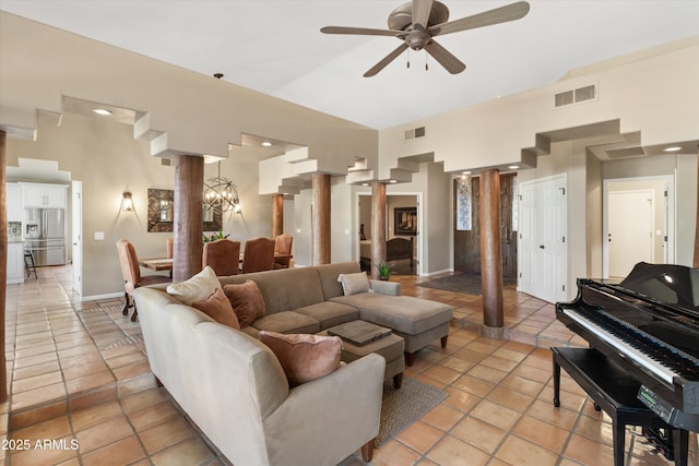 living room featuring light tile patterned floors, ceiling fan with notable chandelier, and decorative columns