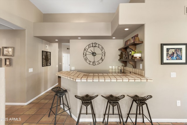 kitchen with dark tile patterned floors, a breakfast bar, kitchen peninsula, and tile countertops