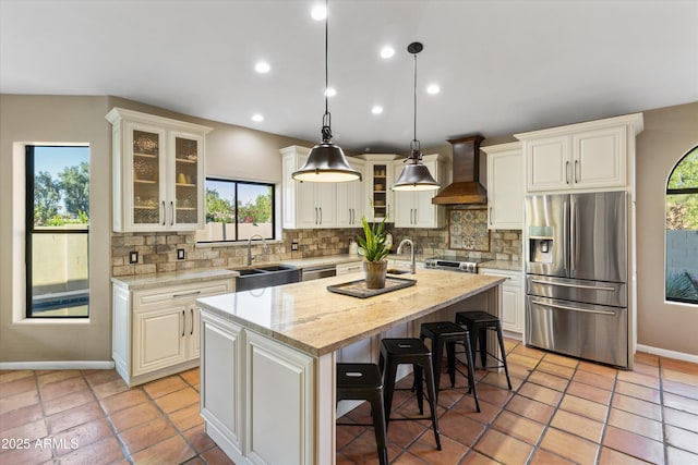 kitchen featuring an island with sink, stainless steel appliances, custom range hood, pendant lighting, and sink