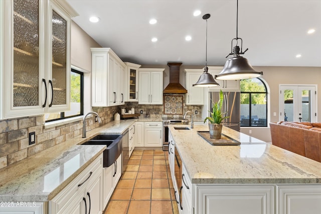 kitchen featuring premium range hood, hanging light fixtures, appliances with stainless steel finishes, and a kitchen island with sink