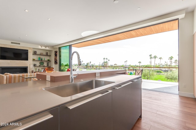 kitchen featuring a fireplace, light hardwood / wood-style flooring, expansive windows, and sink