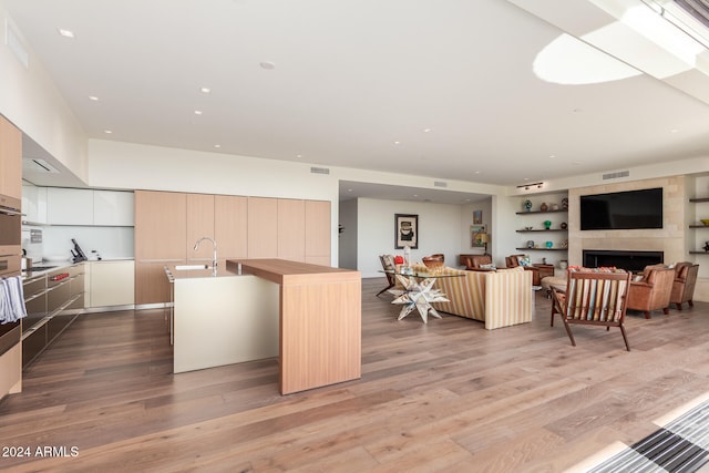 kitchen with light wood-type flooring, sink, a tile fireplace, oven, and an island with sink